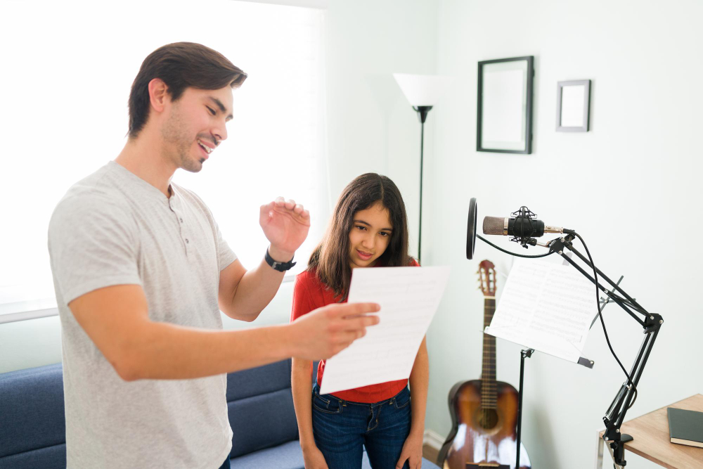 Professor orientando aluna durante aula de canto com partitura e microfone em ambiente de prática musical.