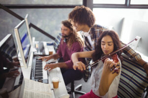 Jovens praticando violino e teclado em ambiente de aprendizagem musical com partituras e equipamentos de áudio.